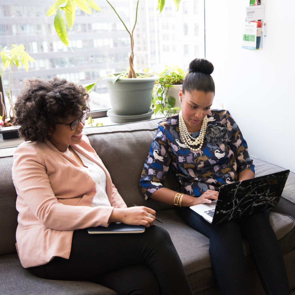 two women sitting on a couch with laptops